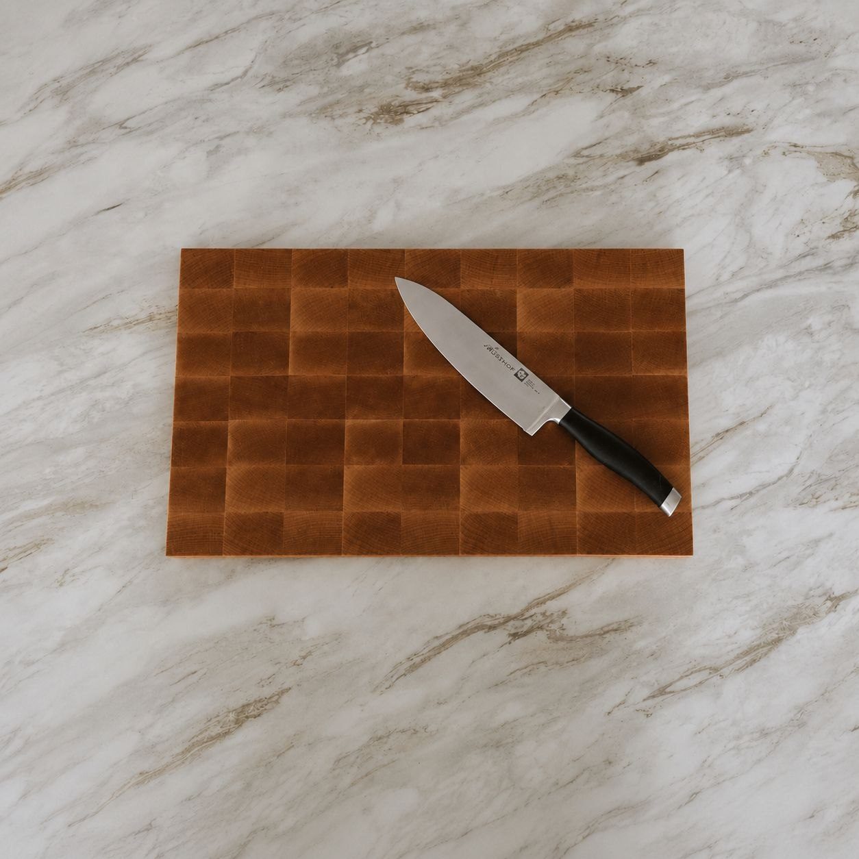 Custom maple end grain cutting board on a marble counter with a chef’s knife